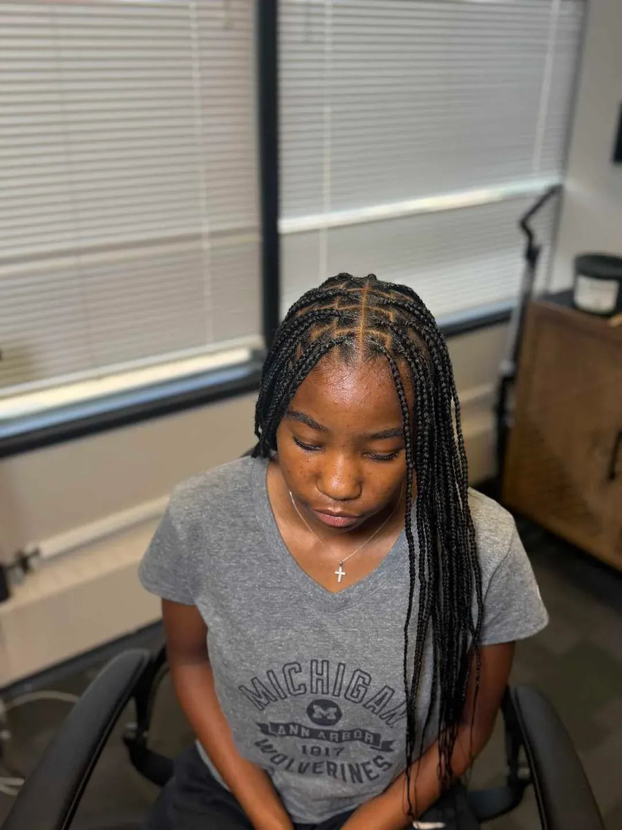 Person with braided hair wearing a gray t-shirt in an indoor setting