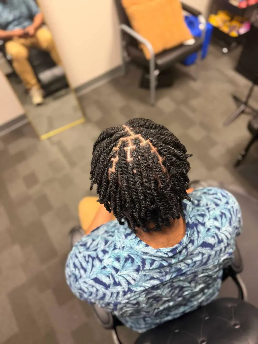 Person with braided hair sitting in a chair in a room with chairs and a table.