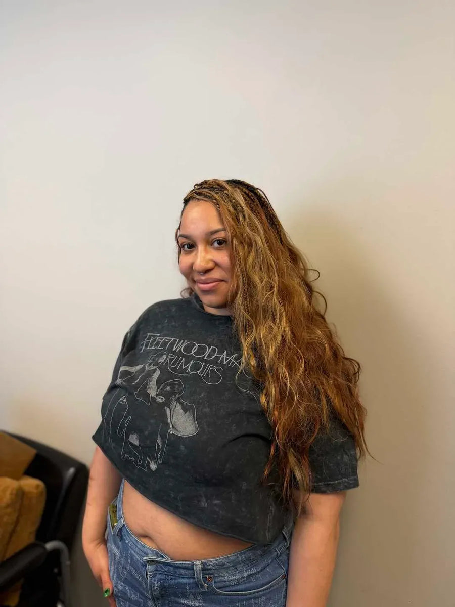 Person wearing a black graphic t-shirt with text and graphics, standing against a plain wall.