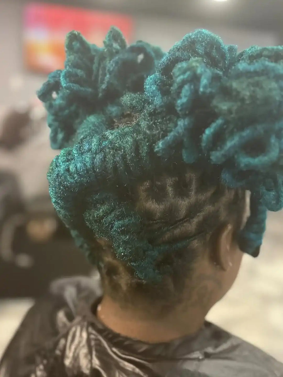 Person with teal-colored hair styled in braids, wearing a gray shirt.