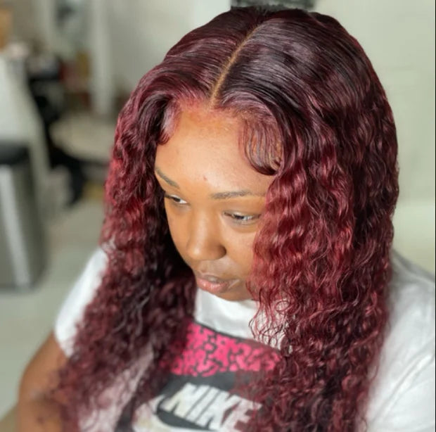 Person with long, red hair styled in loose curls, wearing a white shirt with a graphic design.