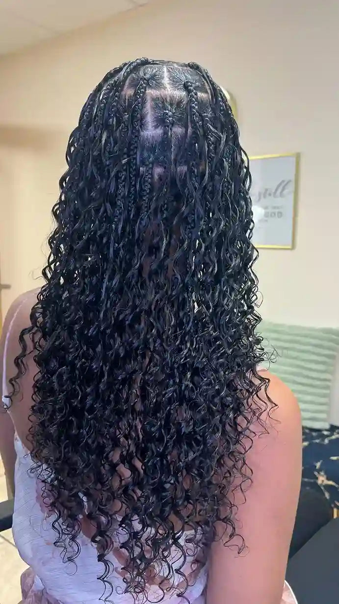Person with long, curly hair styled in a wig, set against a neutral indoor background.