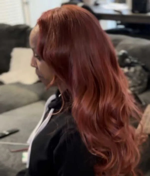 Person with long, wavy red hair sitting on a couch in a living room.