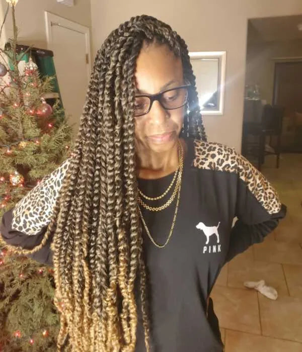 Person with braided hair wearing a black shirt with a logo, standing in a room with a Christmas tree.