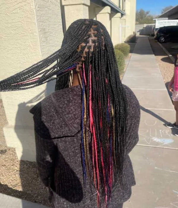 Person with long braided hair standing outdoors on a sidewalk.