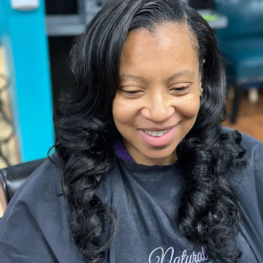 Woman with styled hair wearing a black salon cape with 'Natural' text.