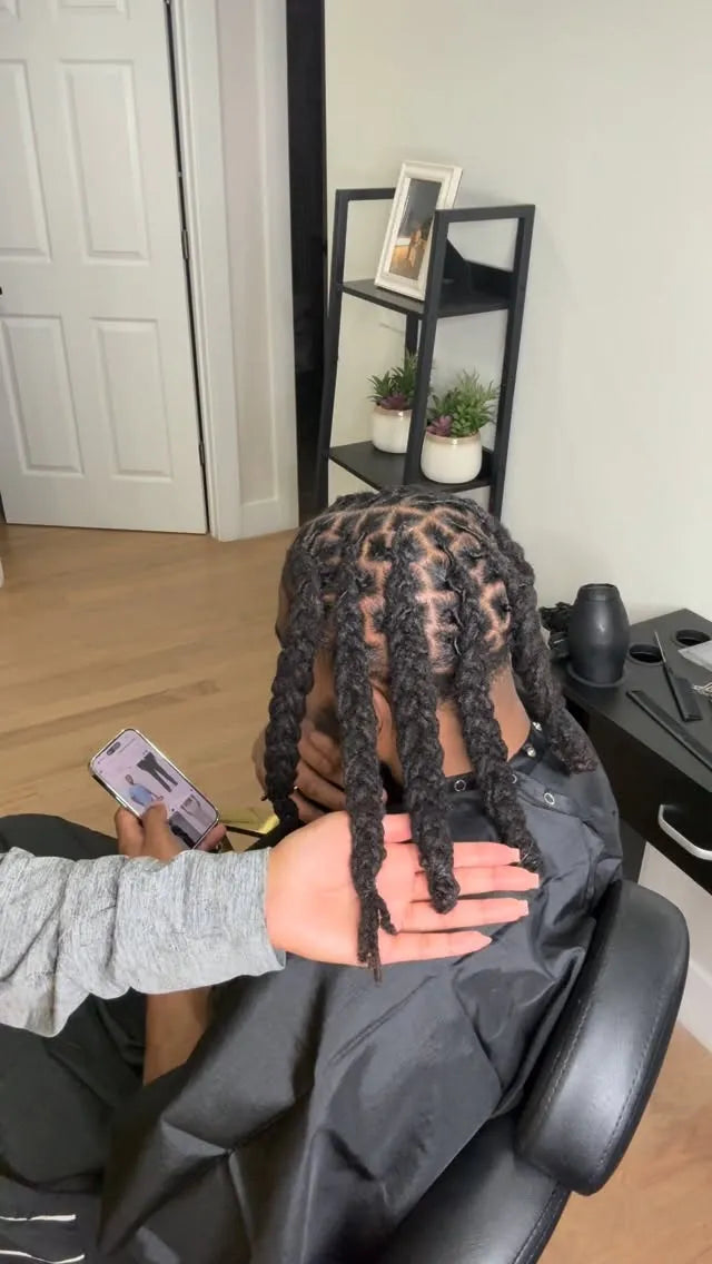 Person with styled hair sitting in a salon chair, holding a phone.