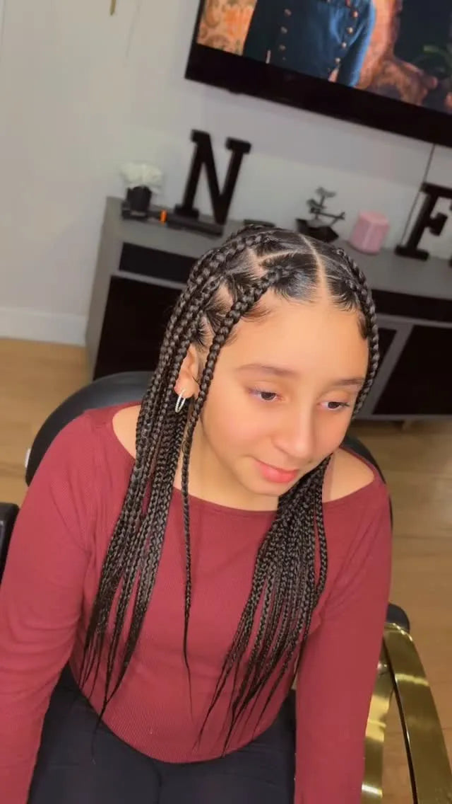 Person with braided hair sitting indoors, wearing a red long-sleeve shirt.