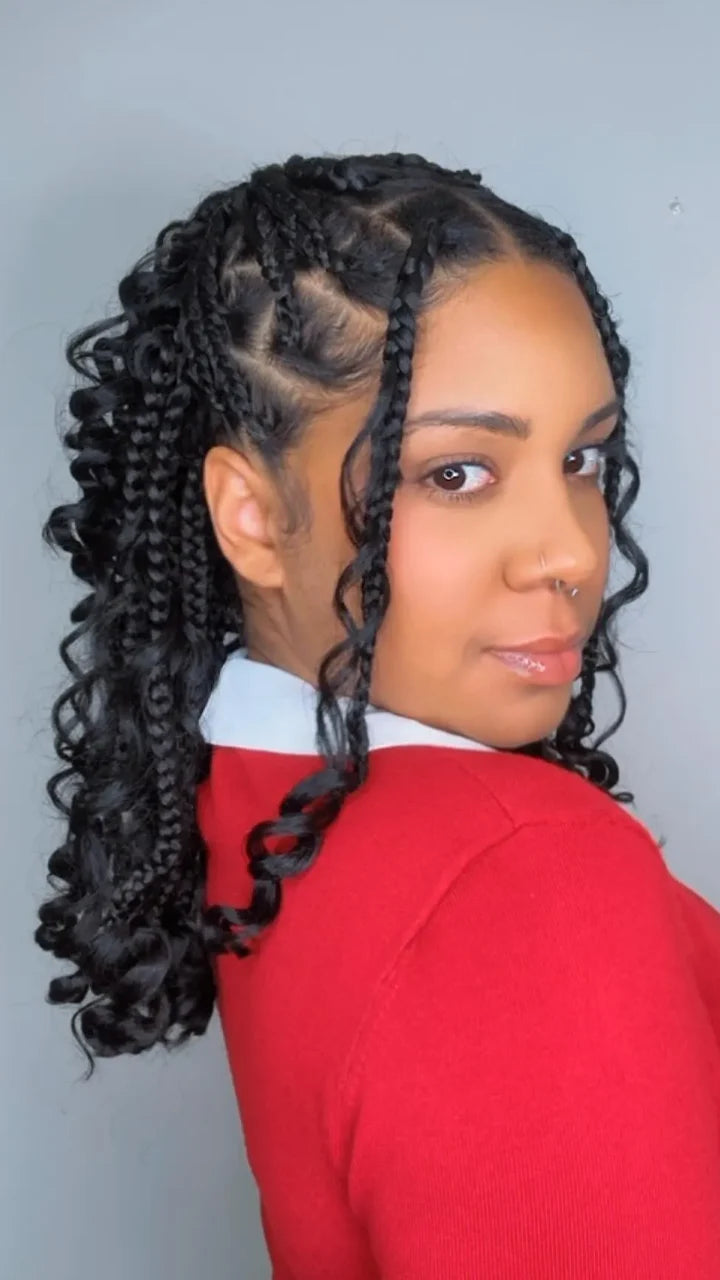 Woman with styled braids wearing a red sweater against a plain background