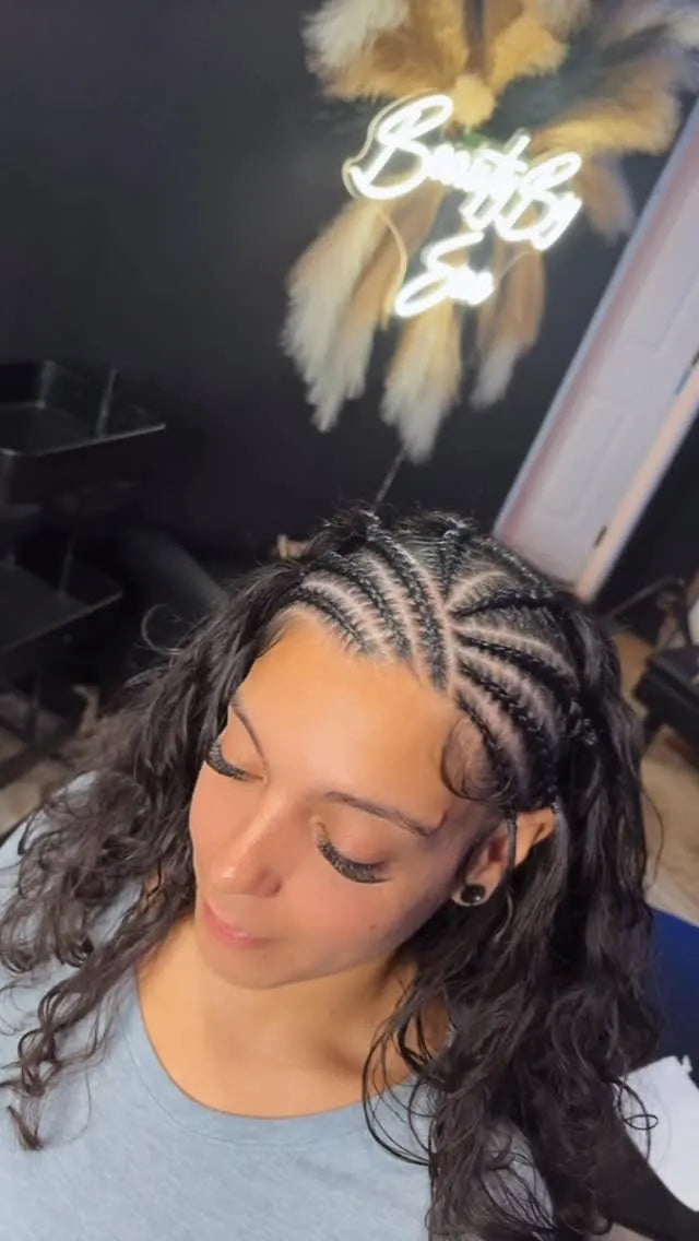 Person with braided hair in a salon setting with a neon sign in the background.