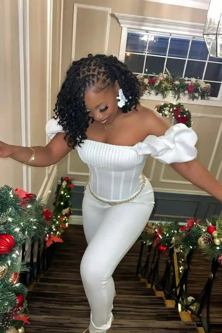 Woman in a white outfit posing in a decorated room with Christmas trees.