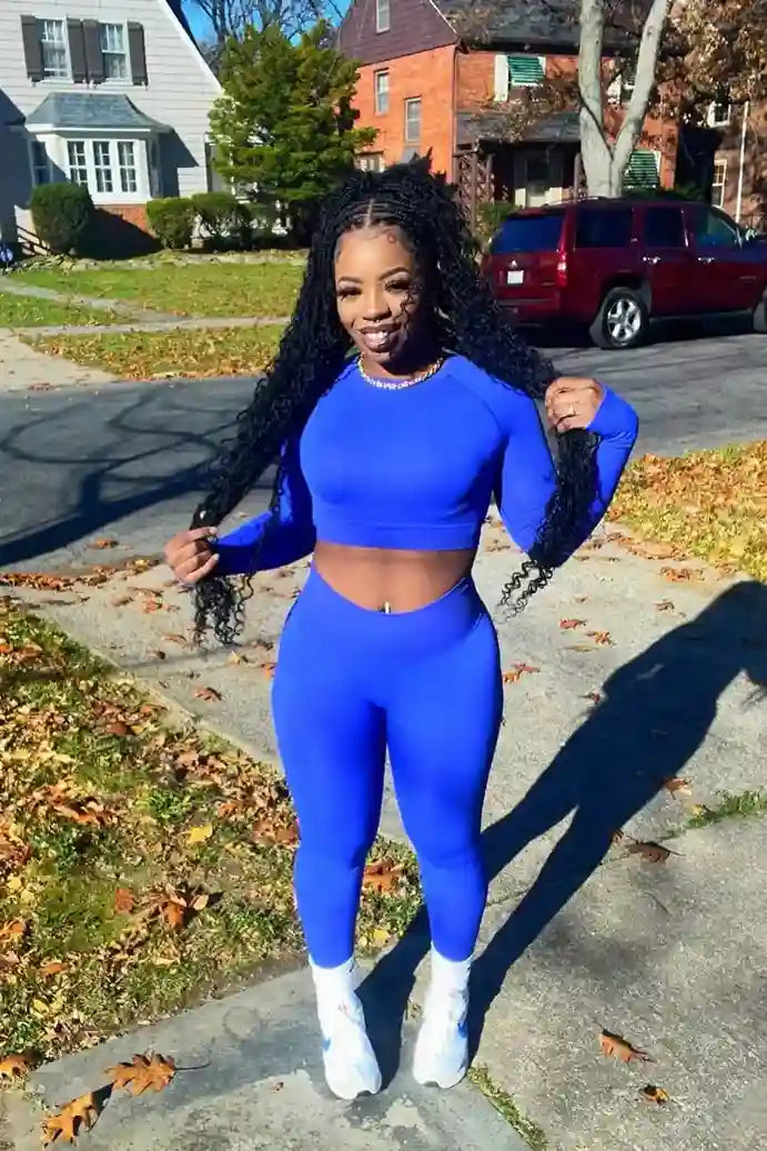 Person wearing a blue athletic outfit standing on a sidewalk with houses and cars in the background.