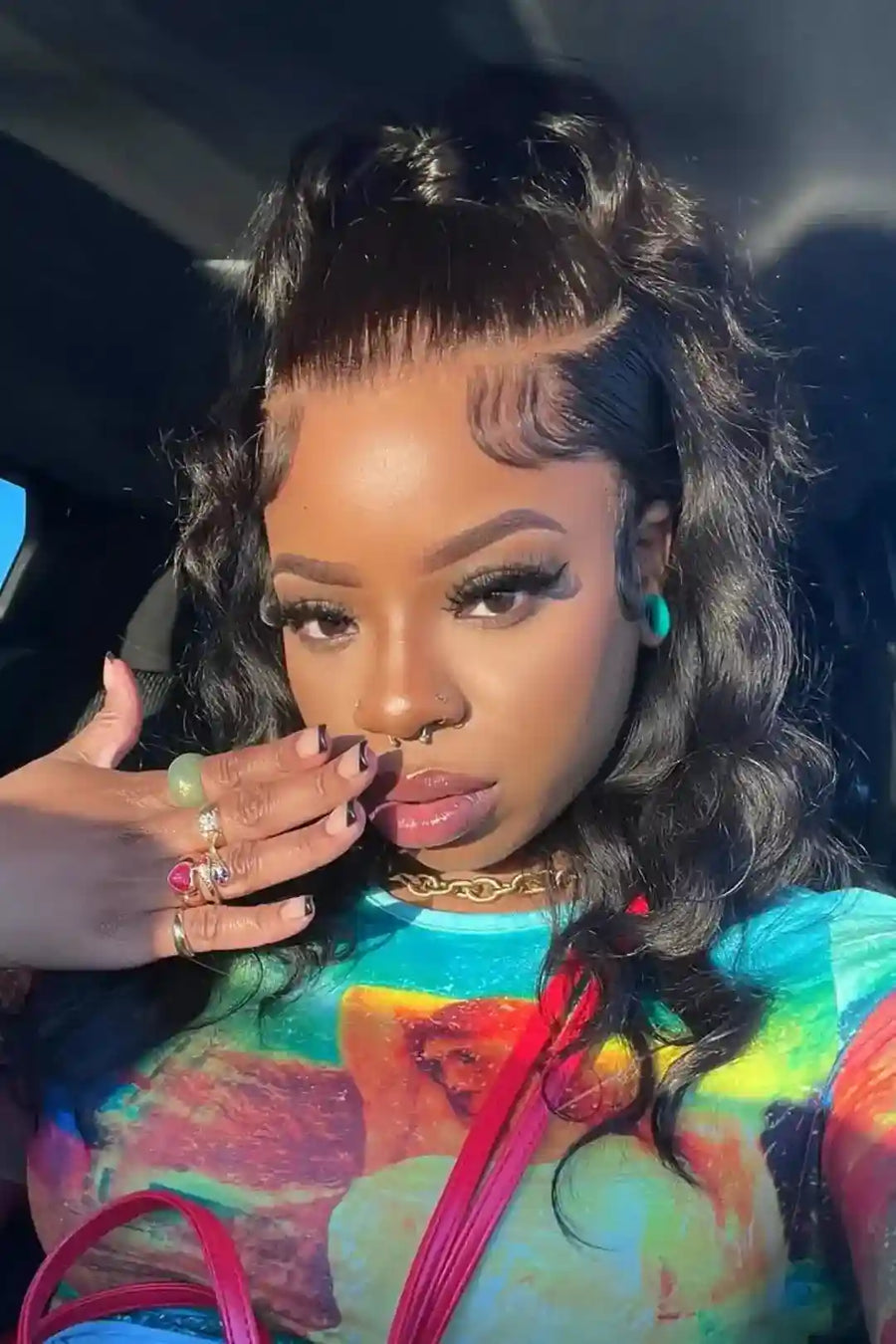 Person wearing a colorful tie-dye shirt with a graphic design, sitting inside a vehicle.