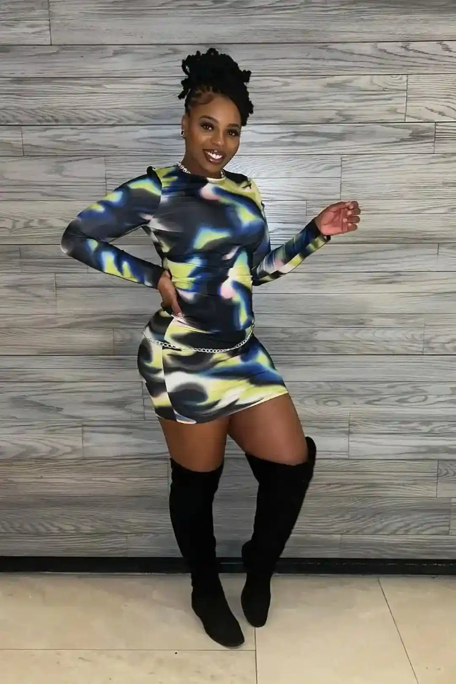 Woman in a colorful dress and knee-high boots posing against a wooden panel background