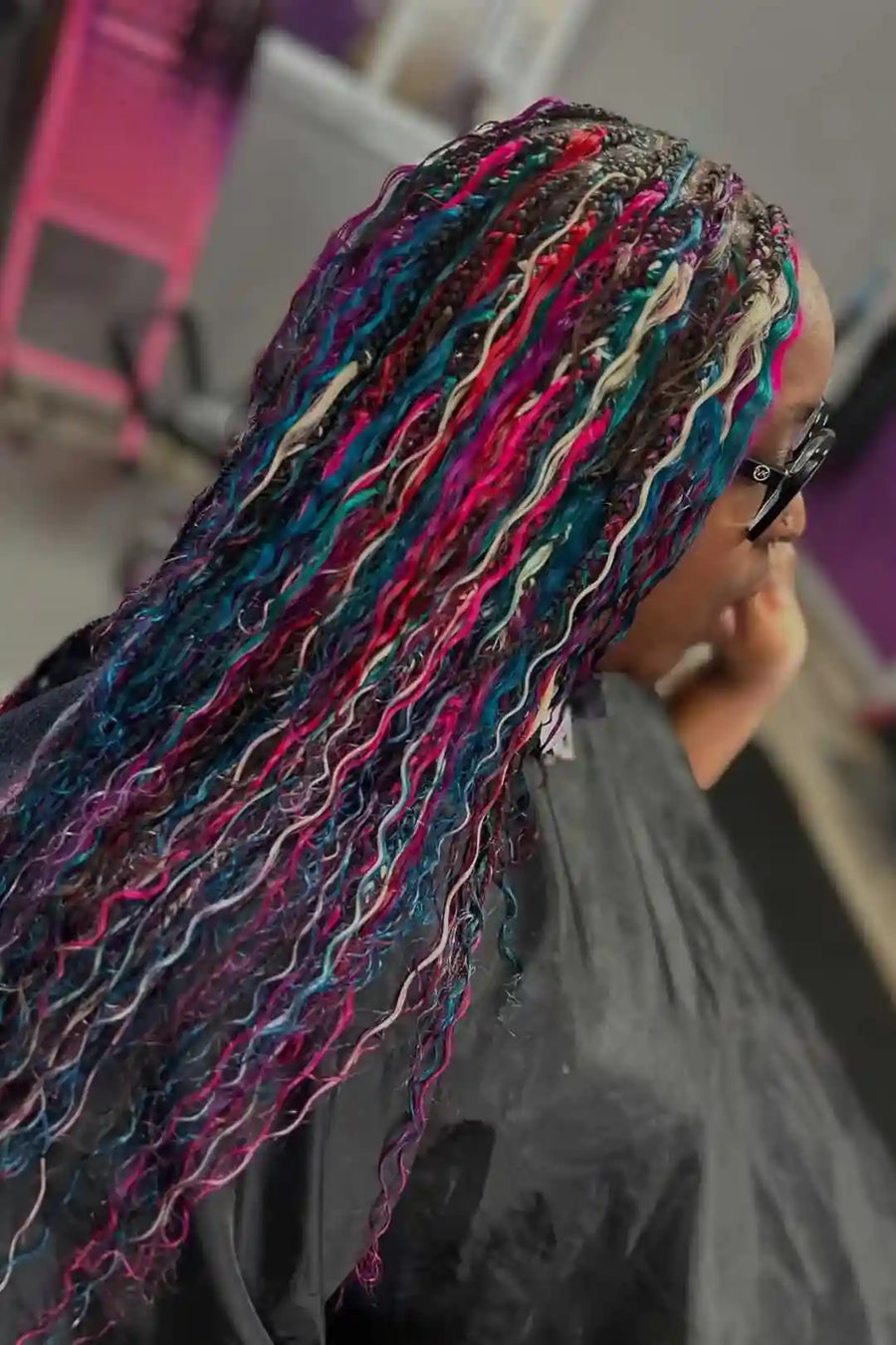 Person with colorful braided hair in a blurred indoor setting