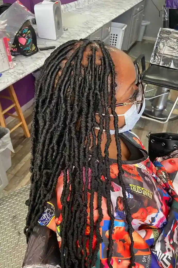 Person with styled dreadlocks wearing a colorful jacket in a salon setting