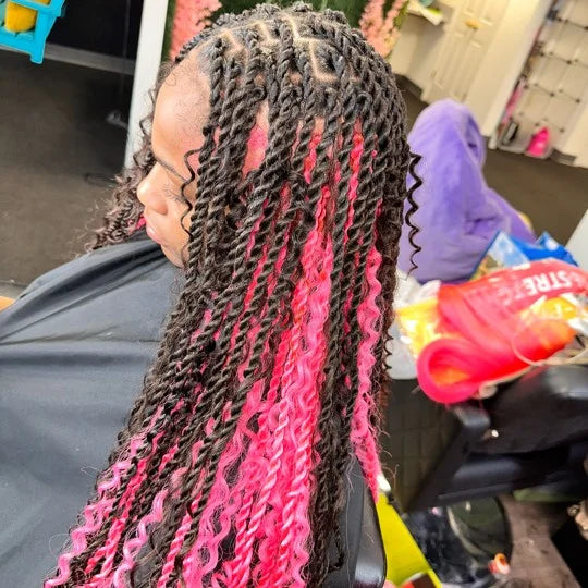 Person with braided hair featuring pink and black colors, sitting in a vehicle.