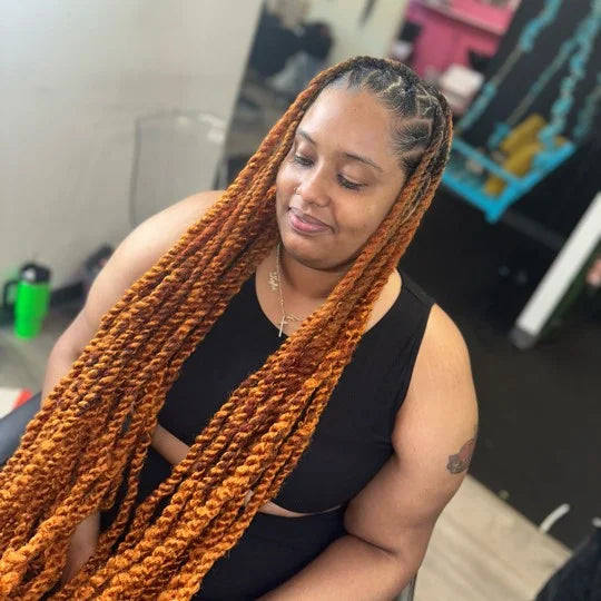 Woman with long orange braids sitting indoors, possibly in a salon.