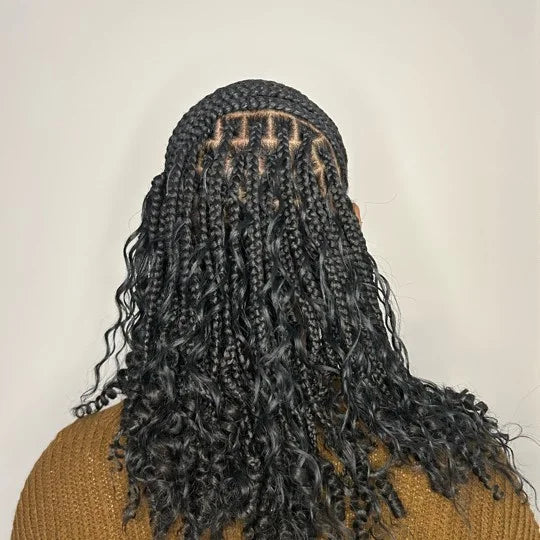 Person with braided hair wearing a mustard yellow sweater on a plain background