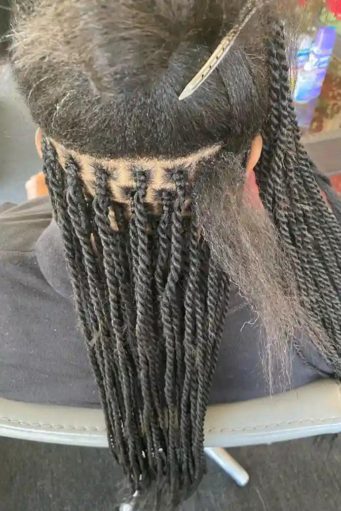 Person with braided hair sitting in a chair, with a blurred background