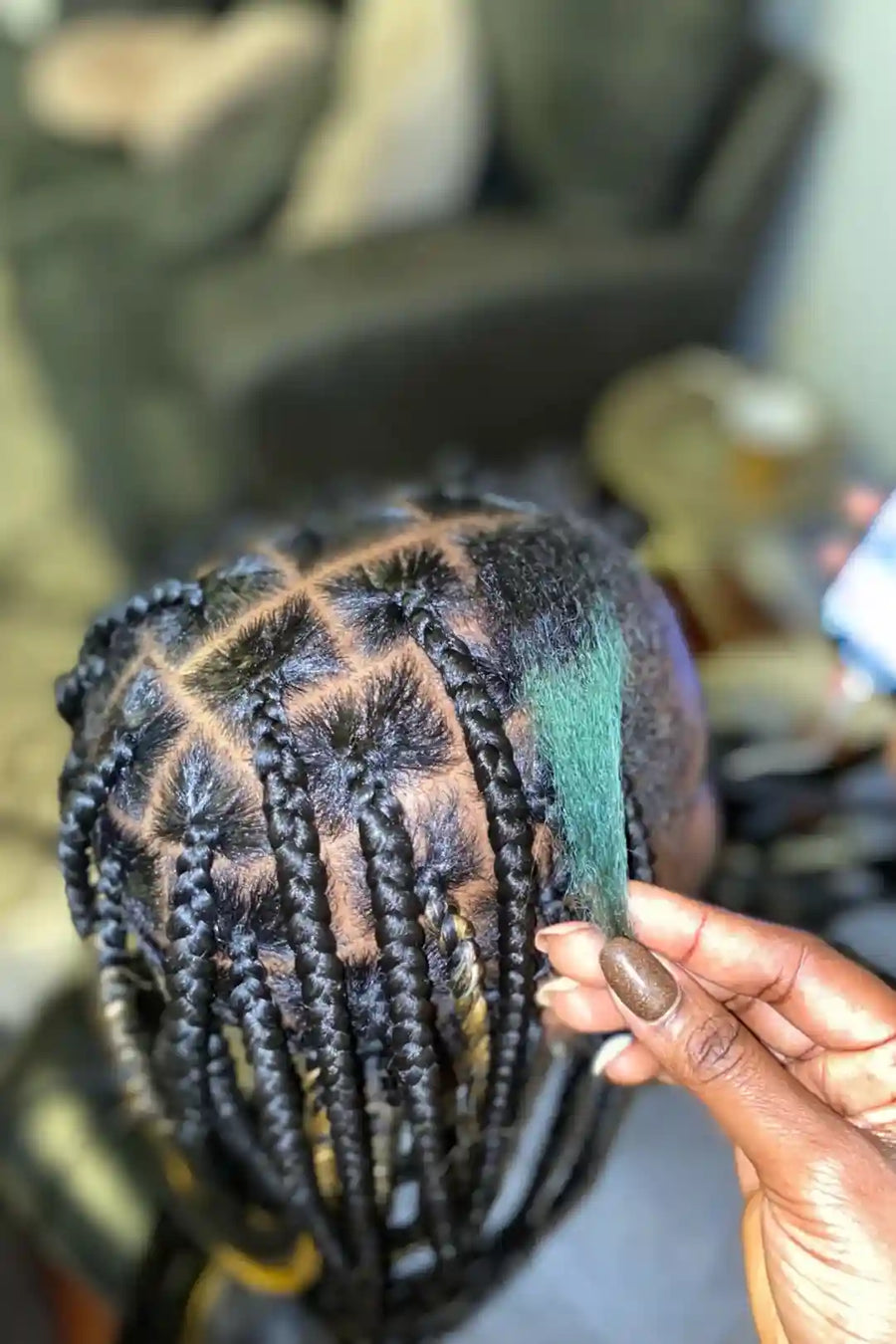 Person with braided hair holding a green section of hair, blurred background