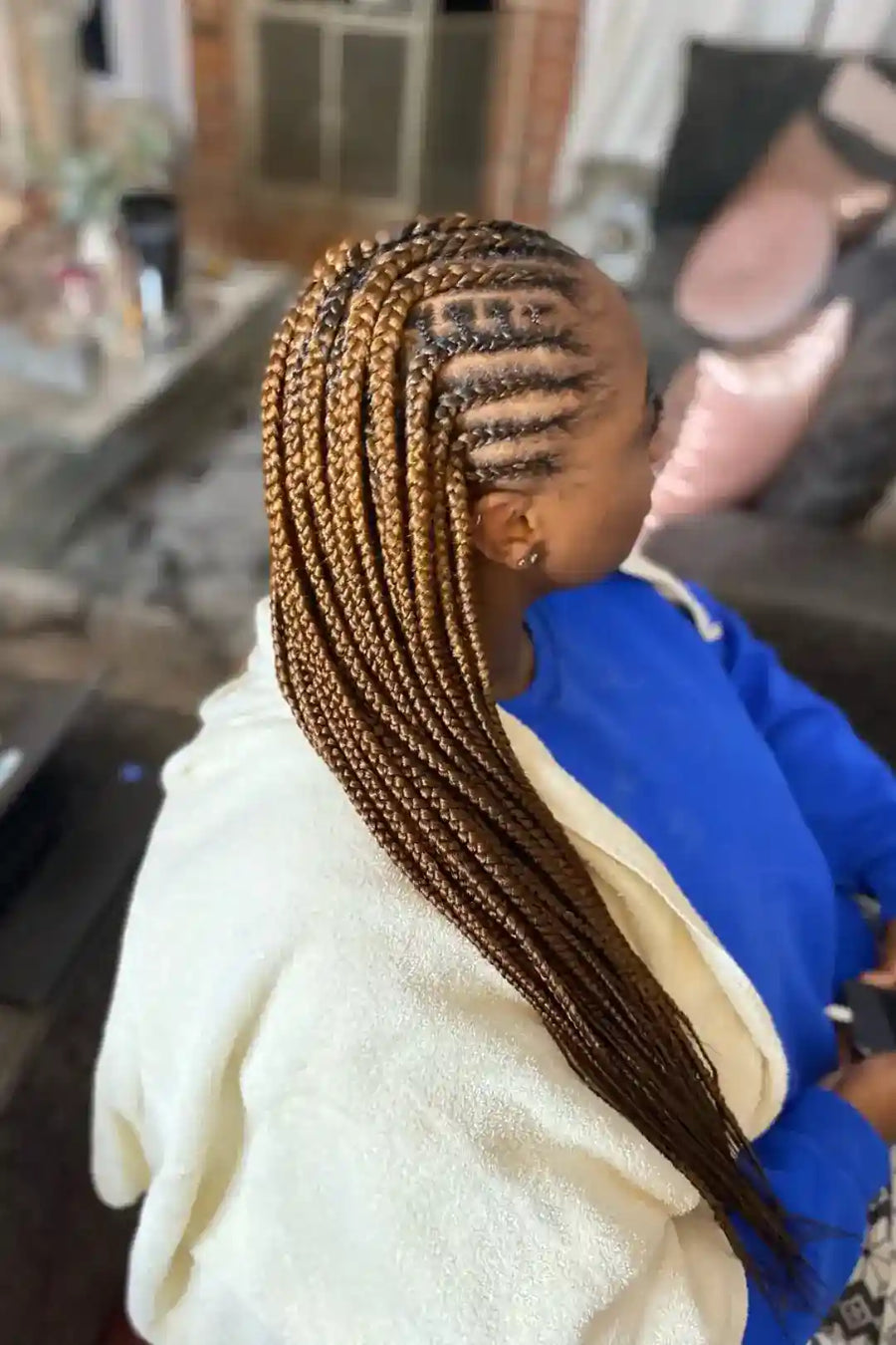 Person with braided hair wearing a white jacket and blue hoodie in an indoor setting.