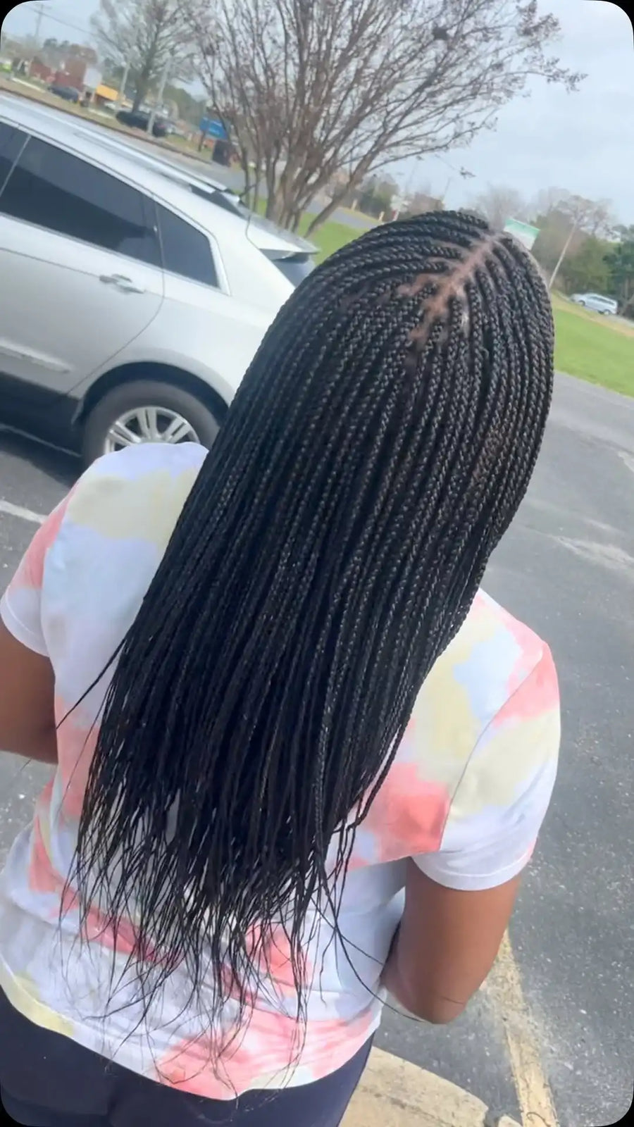 Person with long braided hair standing outdoors on a street.