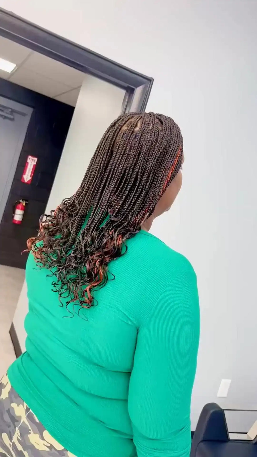 Person with braided hair wearing a green top in an indoor setting.