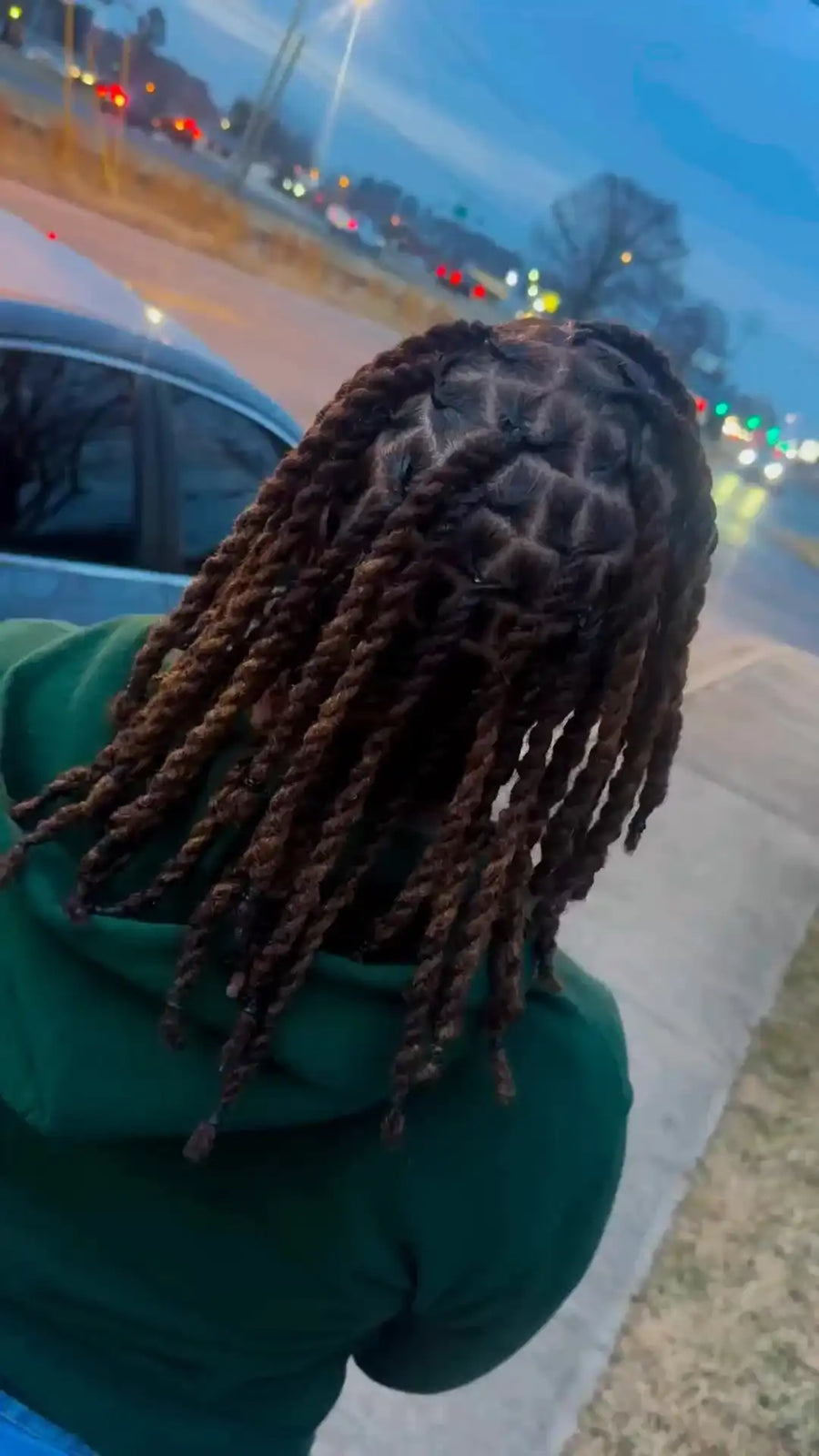 Person with braided hair standing outdoors near a car at night.