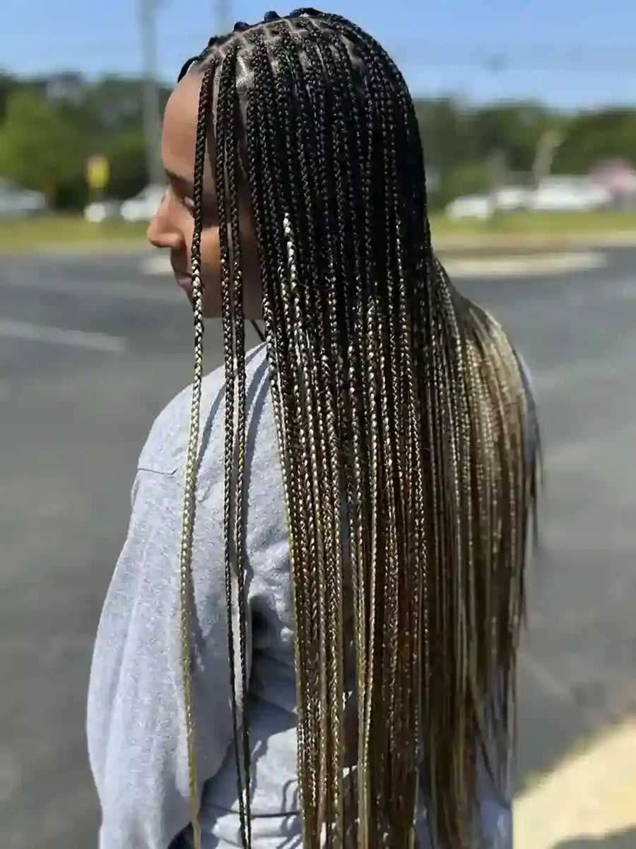 Person with long braided hair standing in a parking lot.