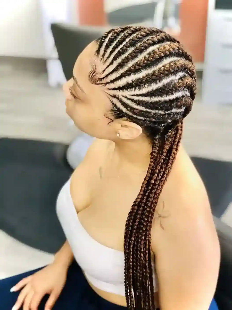 Person with braided hair styled in cornrows, sitting indoors.