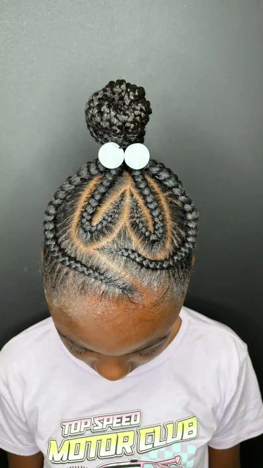 Child with braided hair styled into a heart shape with a bow on a plain background
