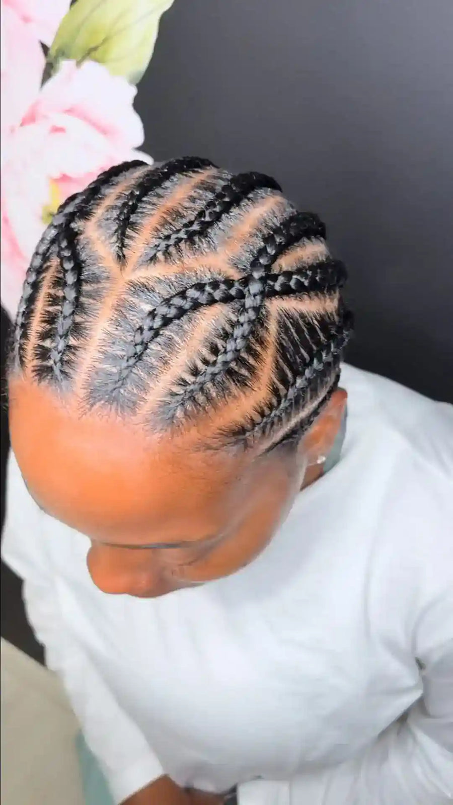Person with braided hair styled in a geometric pattern, wearing a white top.