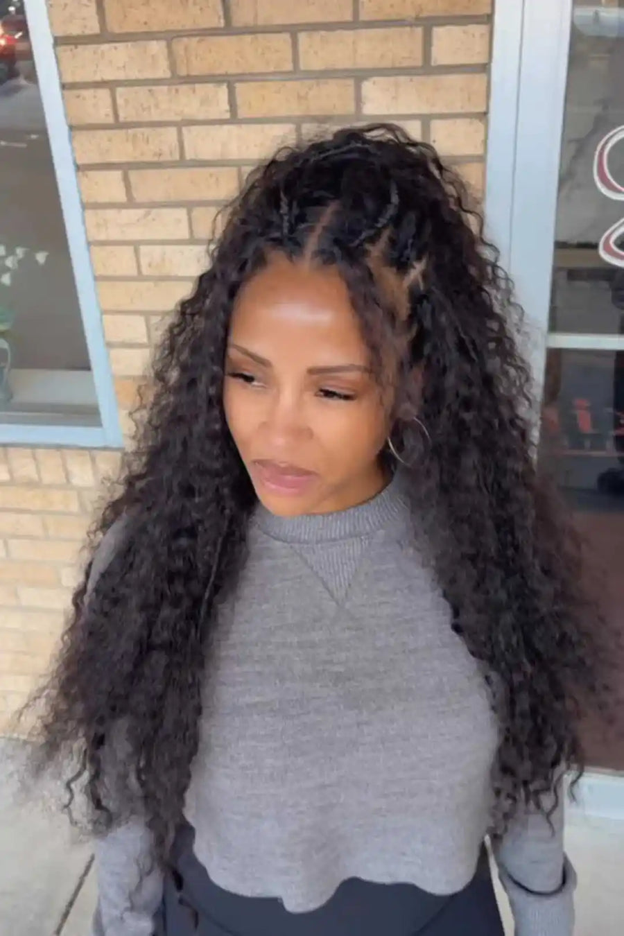 Woman with long, curly hair standing outdoors near a brick building.