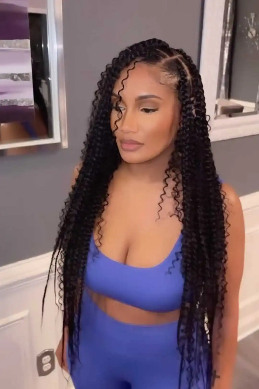 Woman with long, styled hair wearing a blue athletic outfit in a bathroom setting.