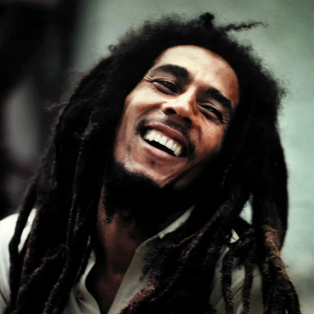 A joyful reggae star Bob Marley with voluminous black dreadlocks smiling.