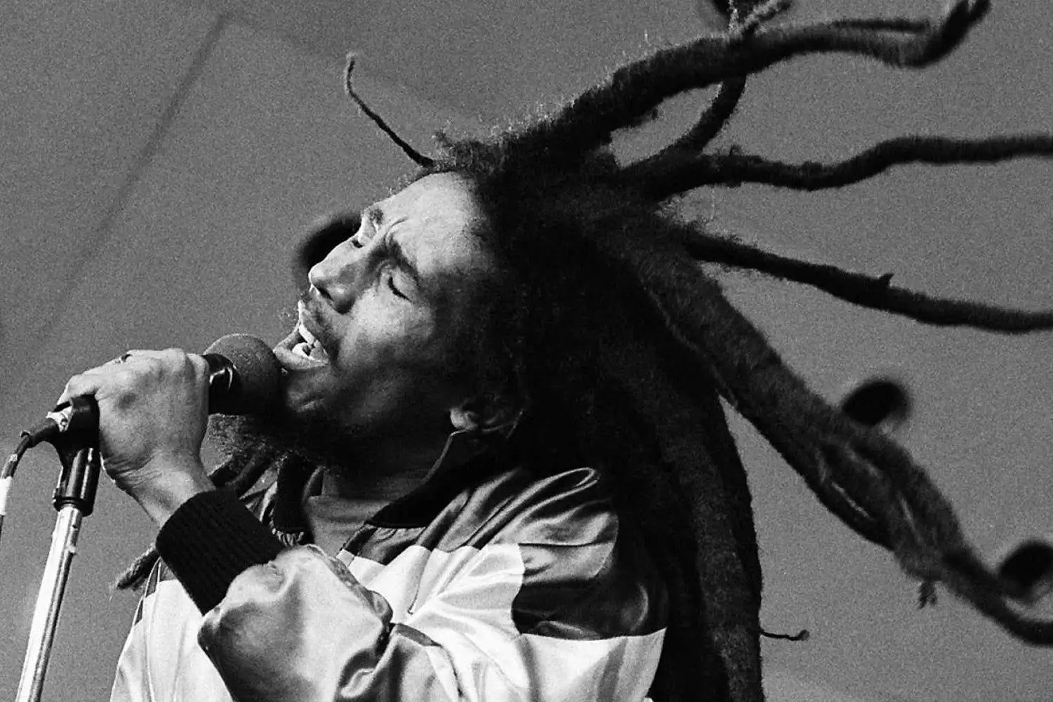 Reggae star Bob Marley singing on a black and white stage, hair flying about.