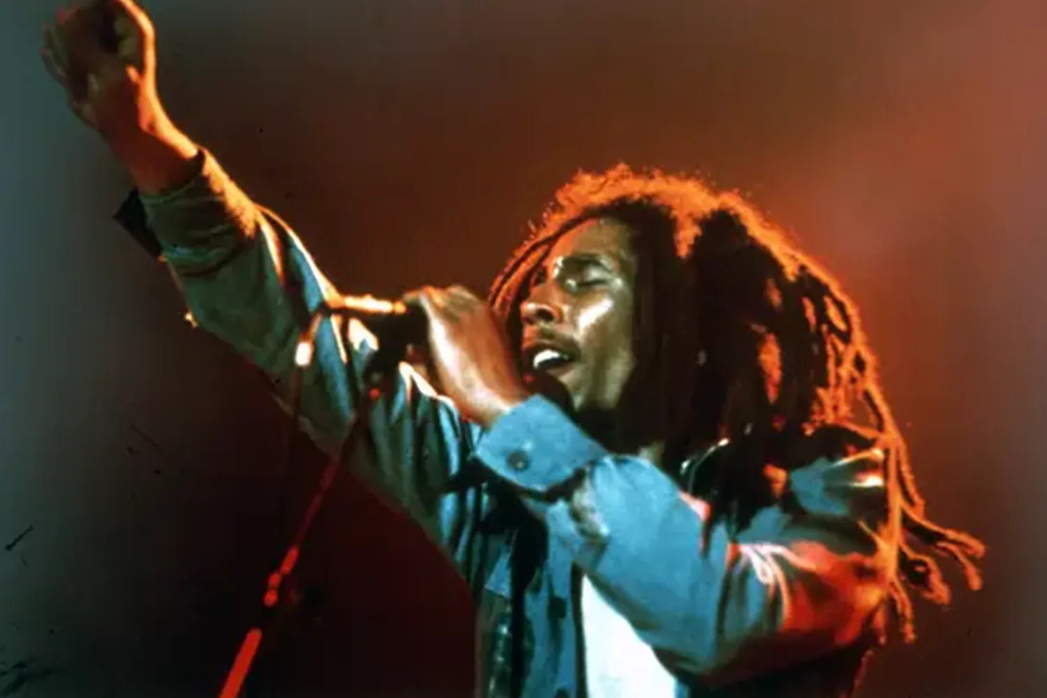 Reggae star Bob Marley performing on stage holding a microphone, wearing a sleek blue jacket.