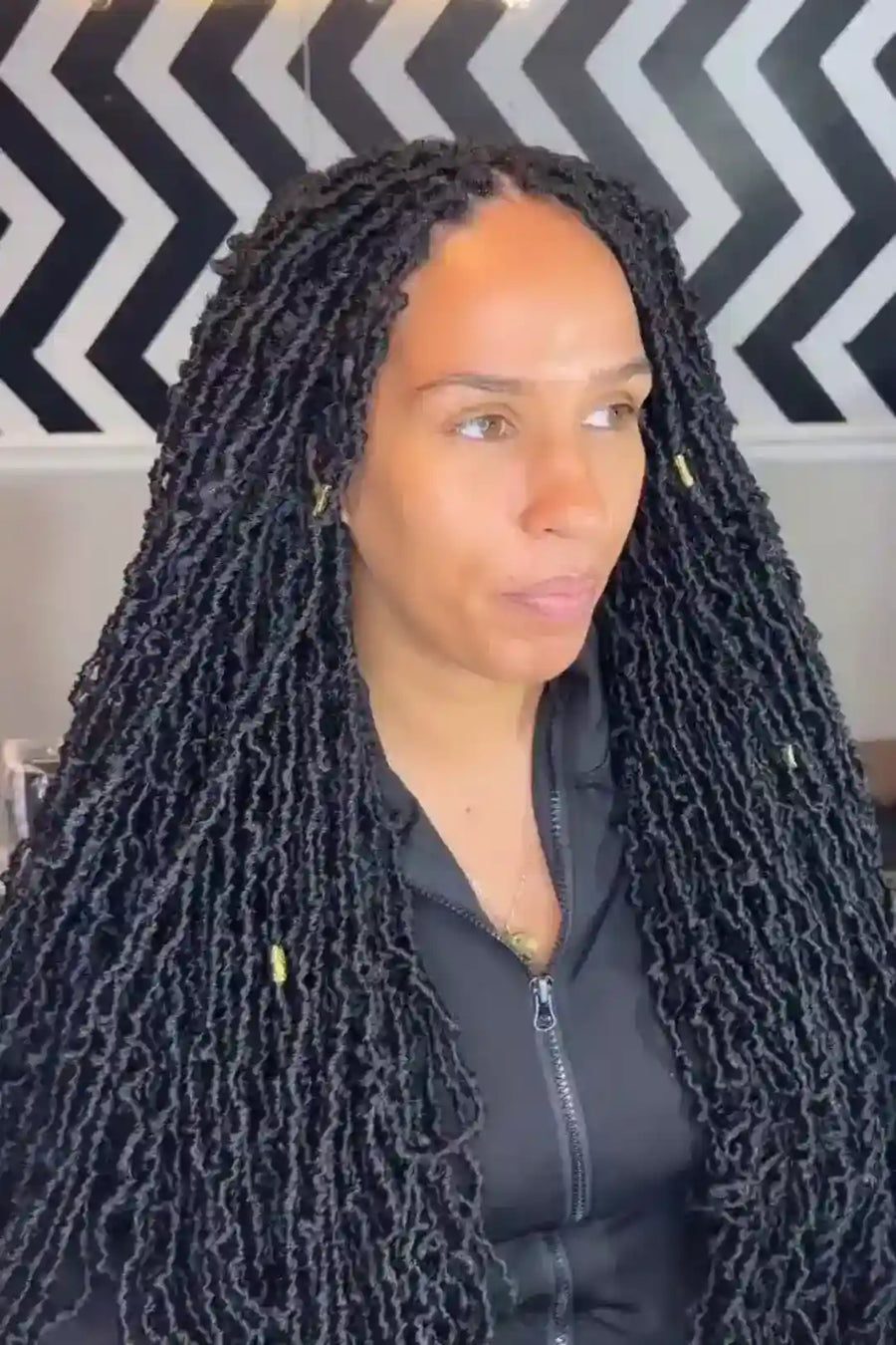 Woman with long braided hair in front of a black and white zigzag patterned wall.