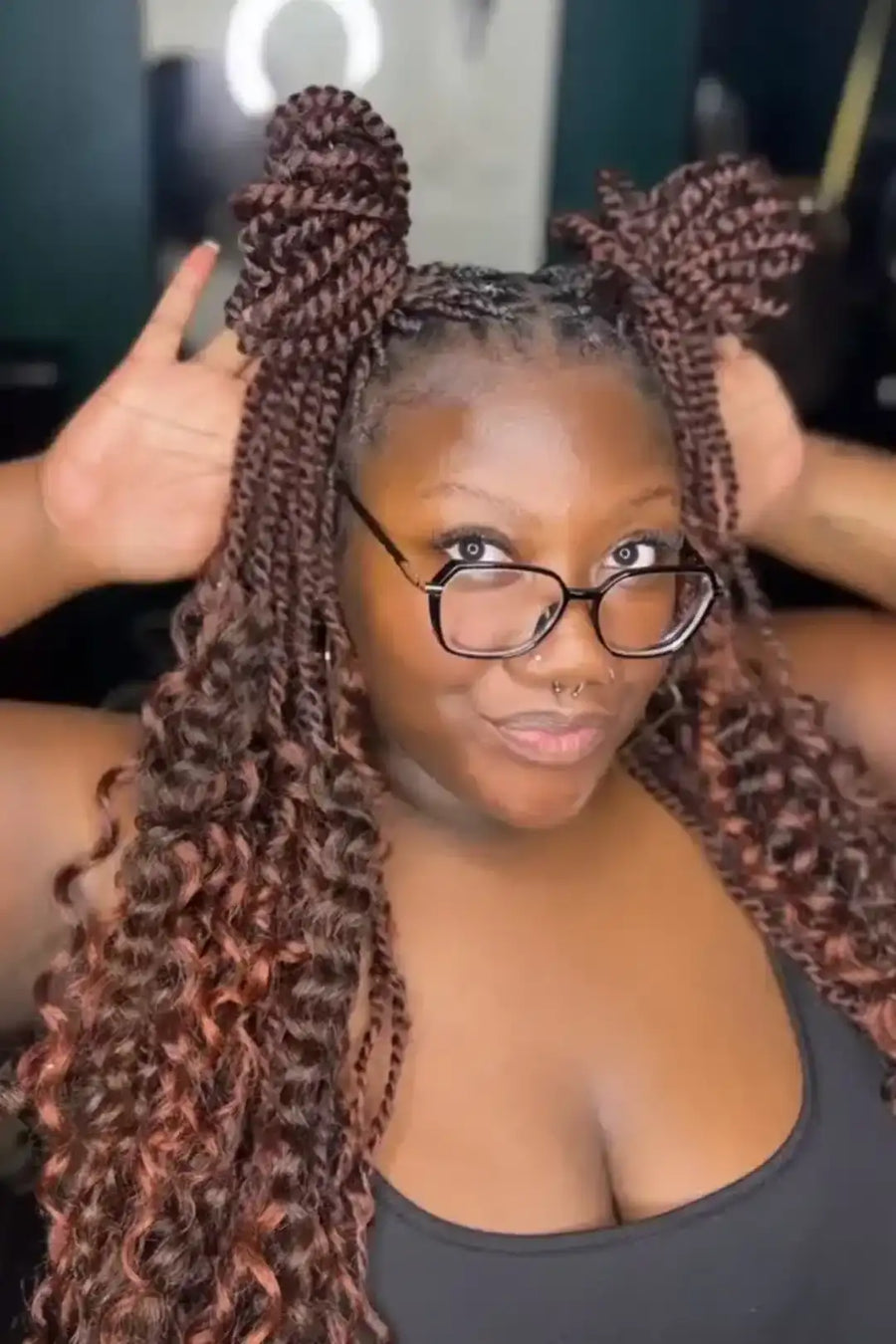 Person with styled hair and glasses, holding braided extensions.