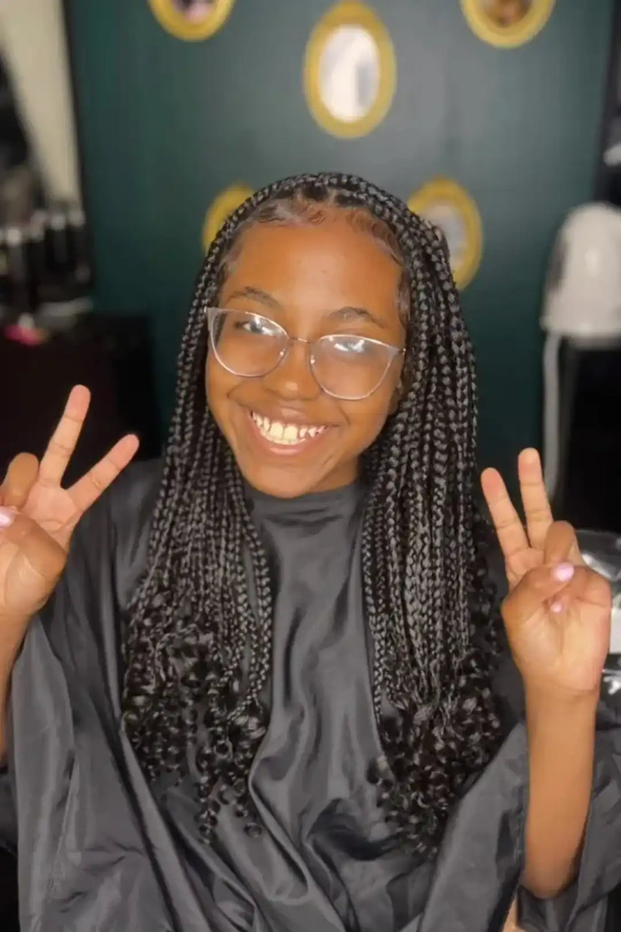 Person with braided hair wearing a gray cape, making peace signs.