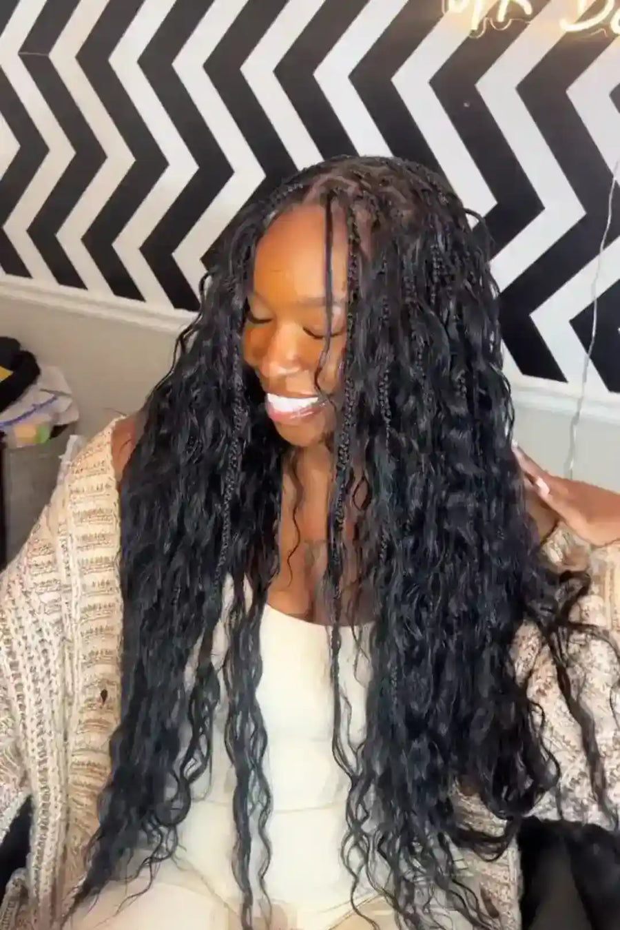 Woman with long, braided hair sitting in front of a black and white zigzag patterned wall.