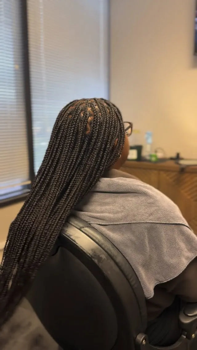 Person with braided hair sitting in a chair, possibly in a salon setting.