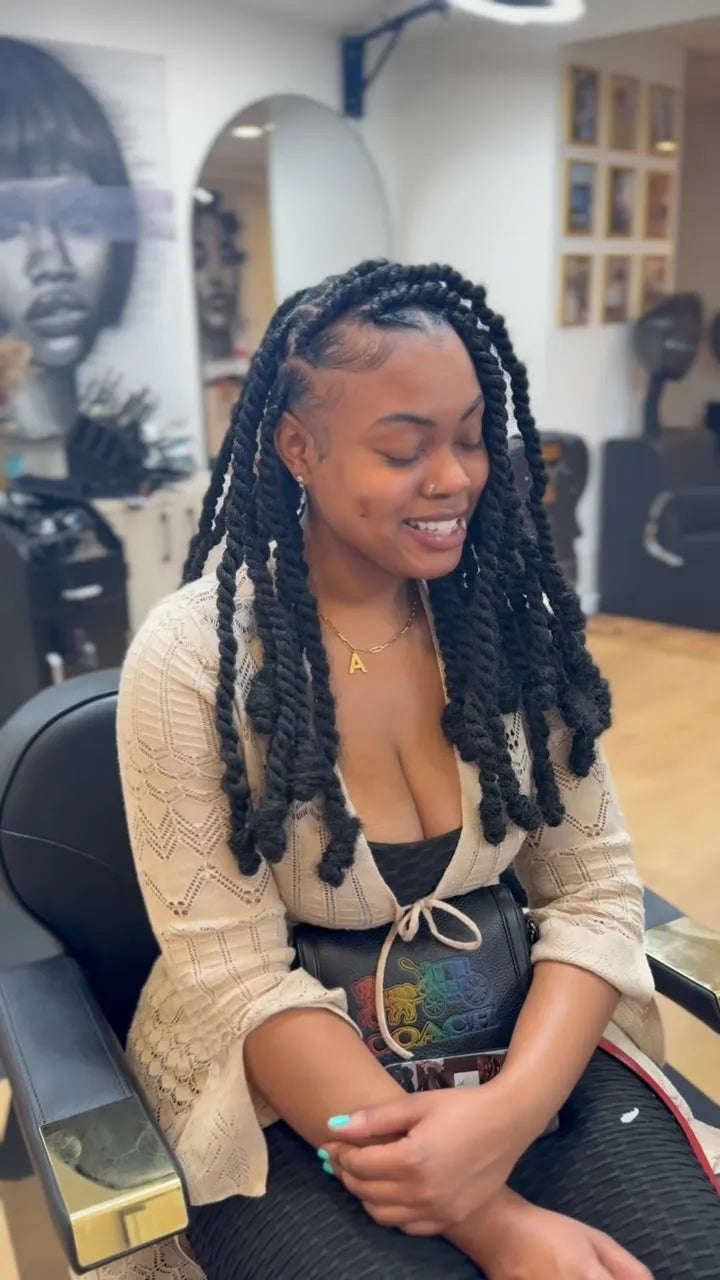 Woman with braided hair sitting in a salon chair, smiling.