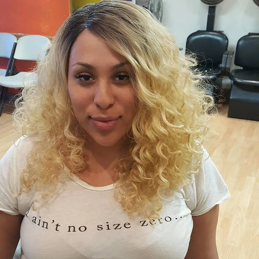 Woman with blonde curly hair wearing a white t-shirt with text in a salon setting