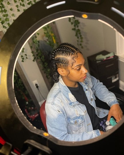 Person with braided hair sitting in front of a round mirror.