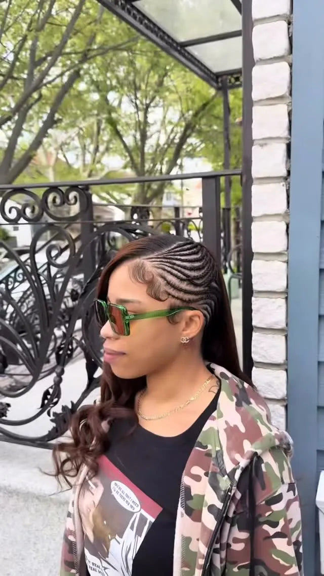 Woman with braided hair wearing sunglasses and a camouflage jacket outdoors.