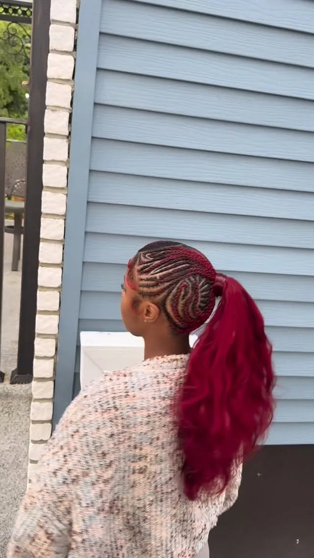 Person with braided hair and a red ponytail standing against a light blue wall.