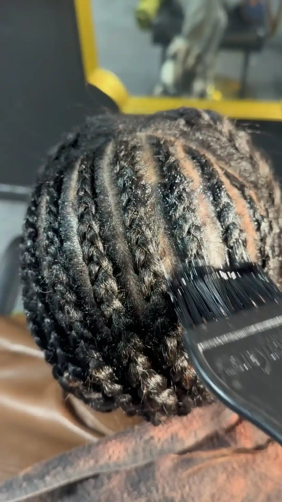 Person with braided hair getting a hair treatment with a brush.