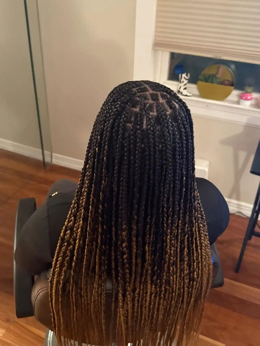 Person with braided hair sitting in a chair in a room with a window and desk.